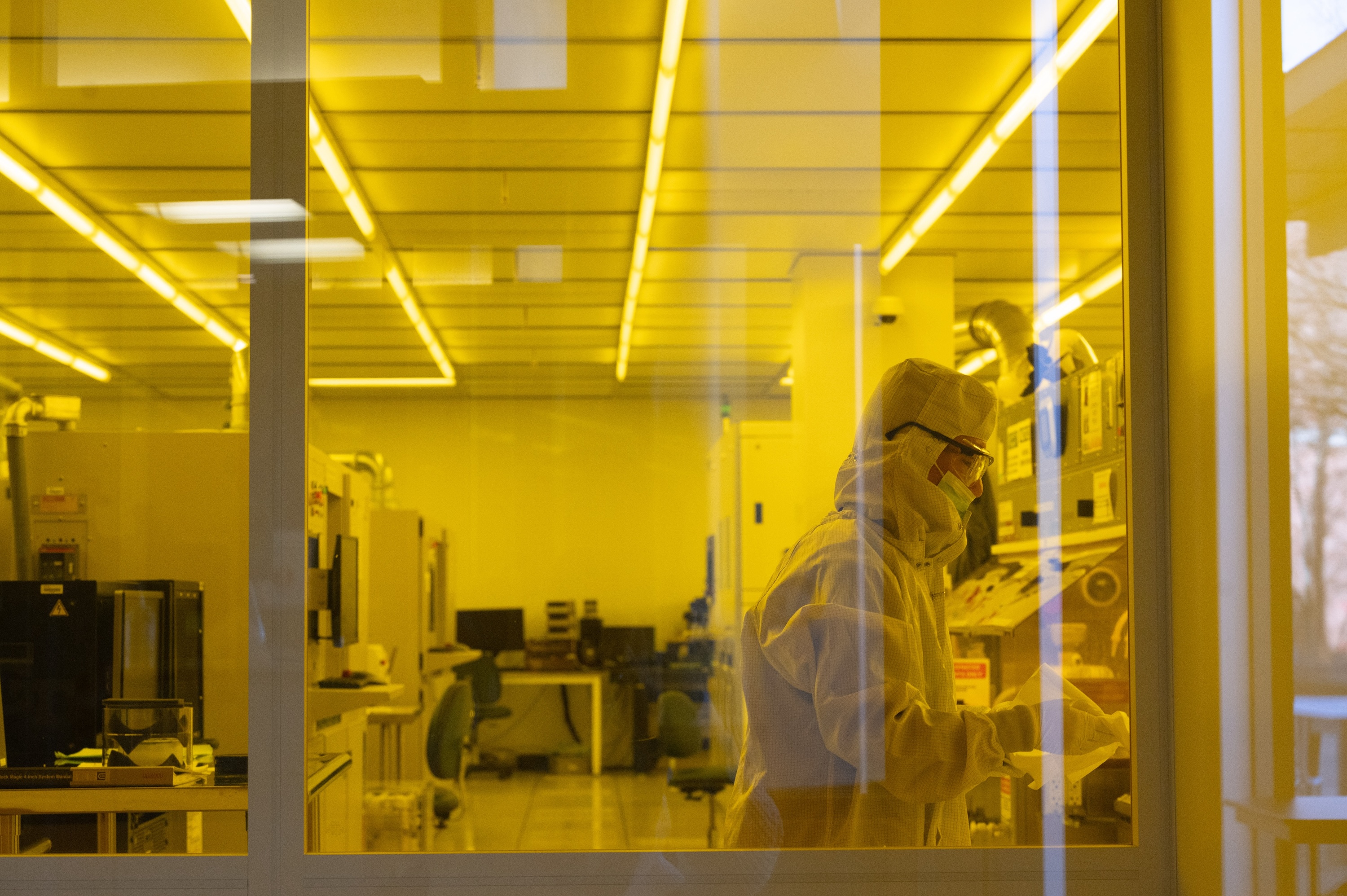 Man in a mask, gloves, and lab coat working at a microscope in a cleanroom