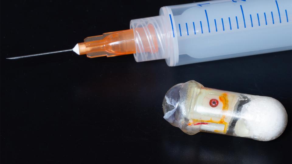 Prototype of an &quot;exploding&quot; capsule next to a syringe. The capsule can deliver medications that are typically only effective if injected.