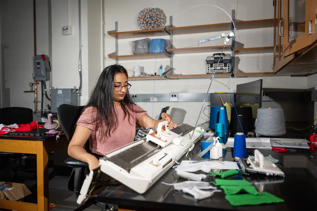 A female student operating a knitting machine in a research lab at Georgia Tech.